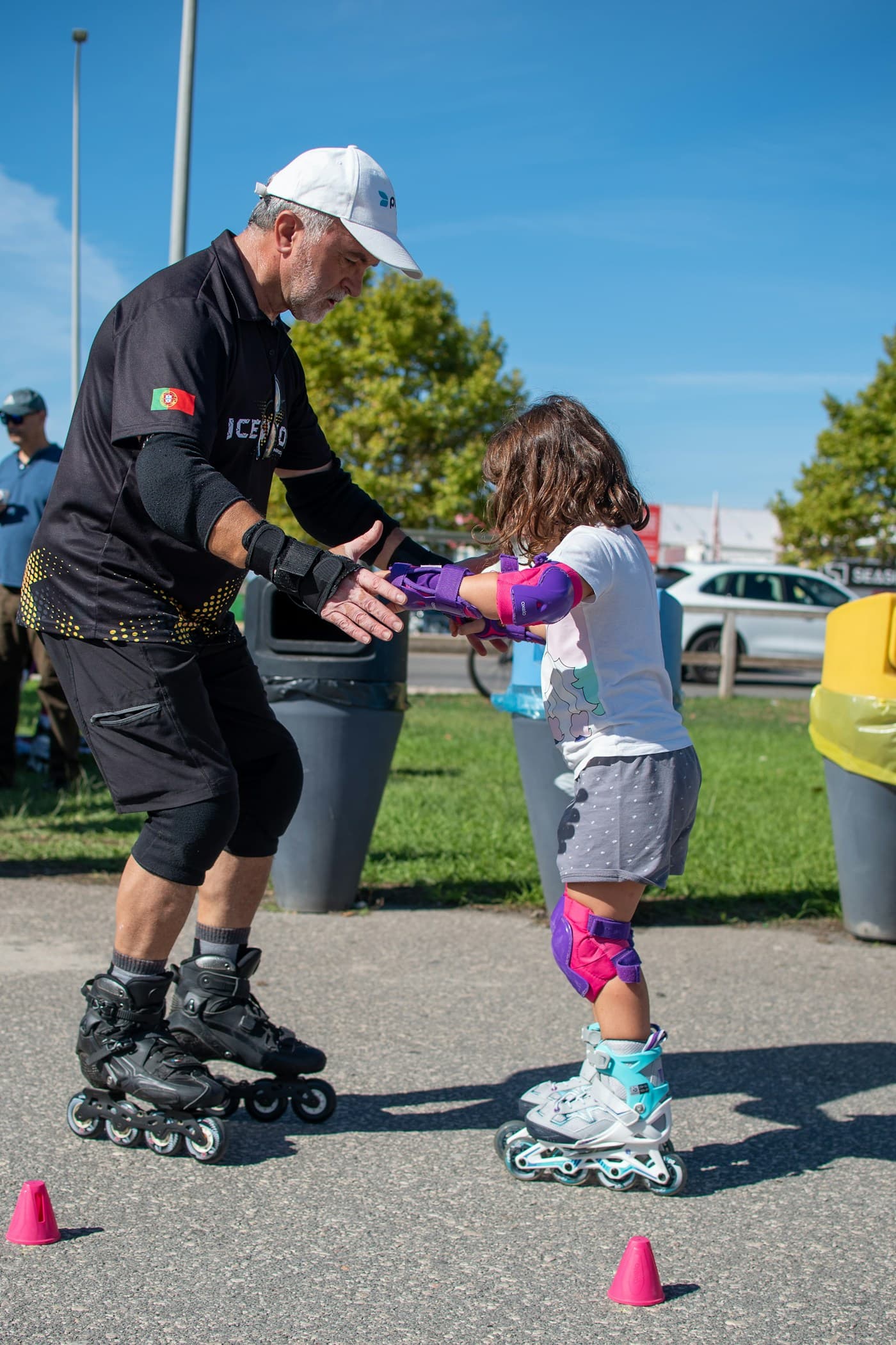A coach holding a young skater's hands as she takes her first glides between training cones