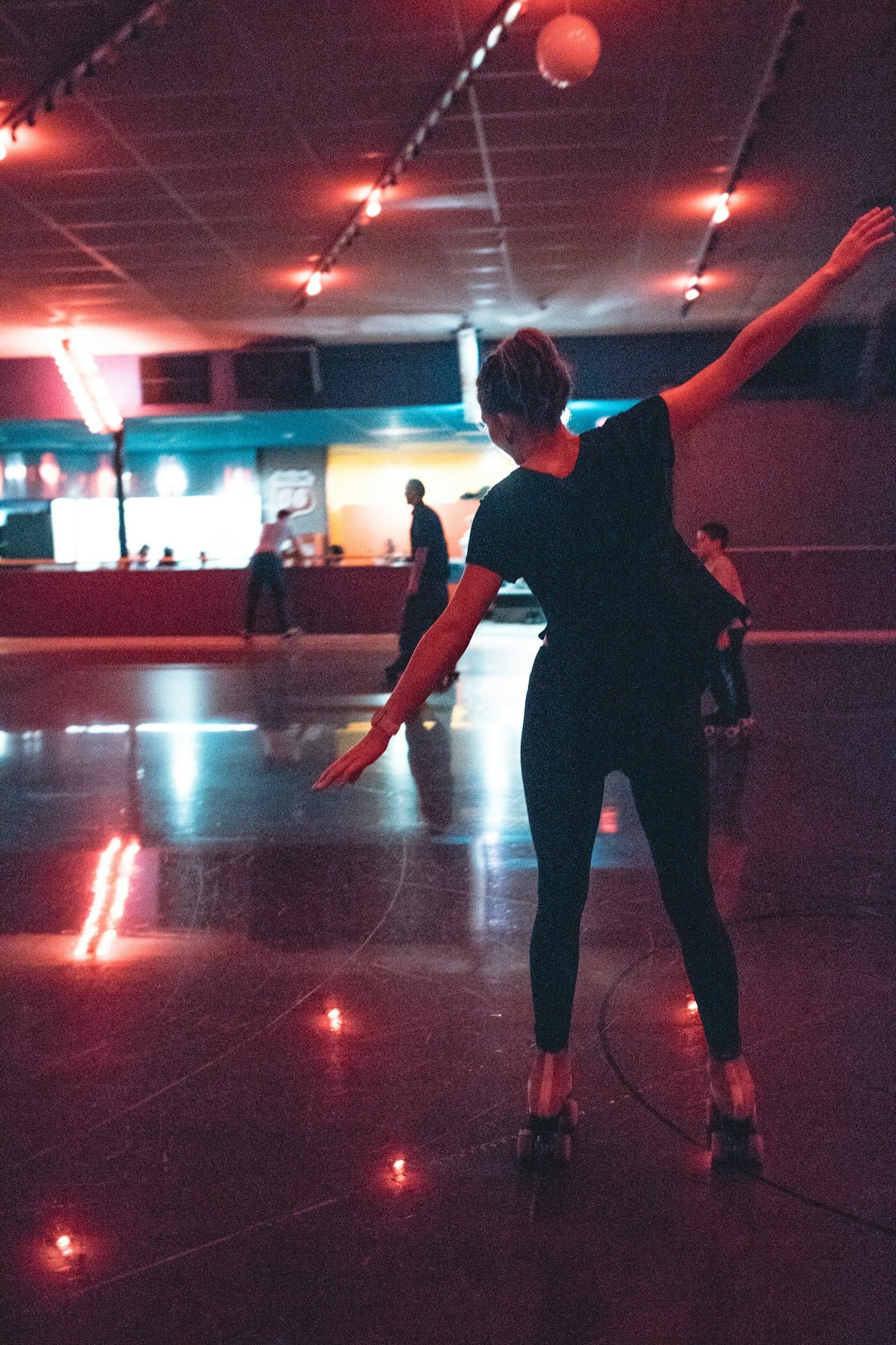 A roller skater performing with arms outstretched under rink lights